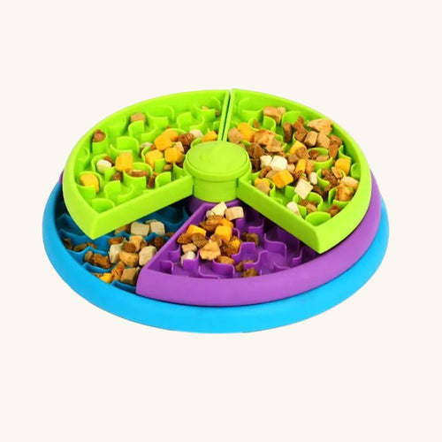 A three-tier slow feeder bowl in green, purple, and blue, each section filled with dry kibble.
